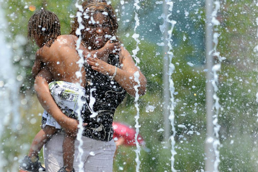 当地时间6月9日，美国巴尔的摩一名妇女抱着孩子在喷泉下乘凉。