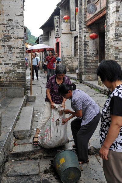 在广西昭平县黄姚古镇景区，几位居民往垃圾桶里倒完垃圾后收起垃圾袋。桶小垃圾多，一个垃圾桶装不下她们的垃圾。