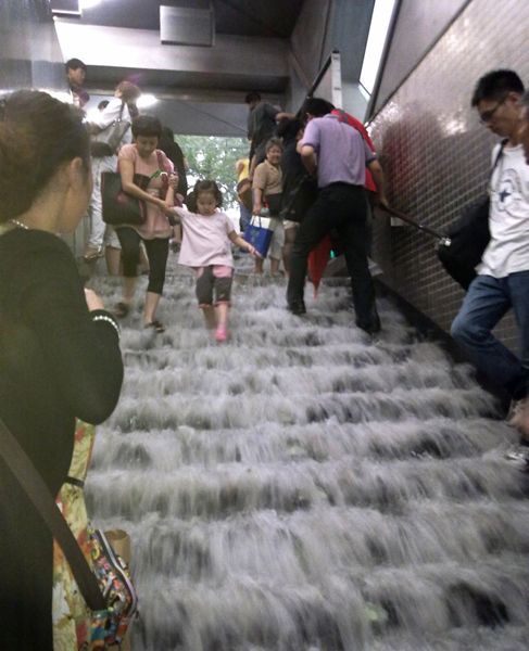 地铁站台内开始限制乘客进入。工作人员表示，由于1号线多个站台积聚了大量乘客，故只能根据车辆行驶状况适当放乘客进入。图为6月23日，在北京地铁4号线陶然亭站内，人们在被雨水冲刷的台阶上行走。