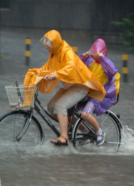 6月23日，北京西城区一所小学附近，一位家长带着孩子在雨中骑行。