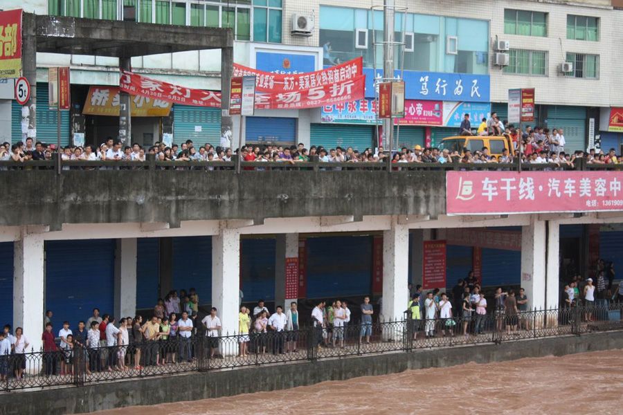 图为河边两崖上万人打着雨伞观看100年大水暴涨。