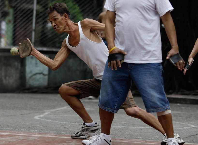 2011年1月23日，菲律宾马尼拉，在一场手球比赛中，一位65岁的老人正在用自己的木头球拍打比赛。他用的比赛用球是从垃圾中回收而来的网球。