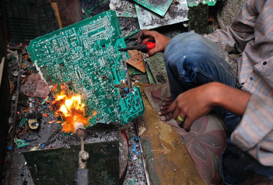 2011年4月20日，巴基斯坦卡拉奇市的一个简易店铺里，一位男子正在处理一块电路板，以从中获取用来制造焊丝的金属。